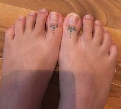 two feet with small tattoos on them sitting next to each other near a wooden table