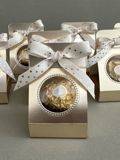 four gold boxes with white bows and chocolates in them