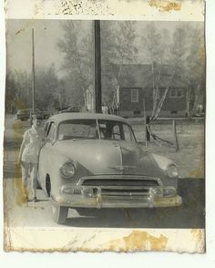 an old black and white photo of a man standing next to a car in front of a gas station