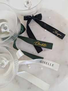 three wine glasses sitting next to each other on top of a white tablecloth with black ribbon