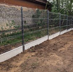 a fence that is next to a building with dirt on the ground in front of it