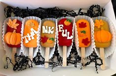 four decorated pops are in a box with black lace and pumpkins on the sides