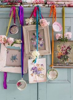 an assortment of framed pictures hanging on a blue wall with ribbons attached to the hooks