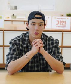 a young man sitting at a table with his hands folded in front of the camera