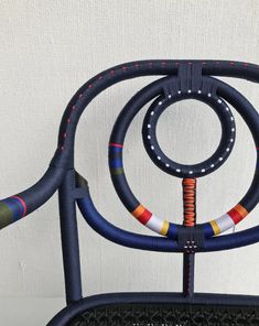 a chair made out of woven material with colorful rings on the back and sides, sitting in front of a white wall