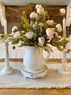 a white vase filled with flowers sitting on top of a table next to two candles