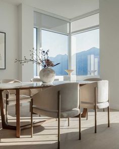 a dining room table with chairs and a vase on top of it in front of large windows