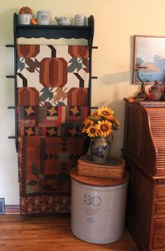 a vase filled with yellow flowers next to a quilted wall hanging on the wall