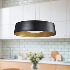 a black and gold pendant light hanging over a kitchen table with flowers in the foreground