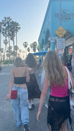 two women walking down the street in front of a store with palm trees behind them