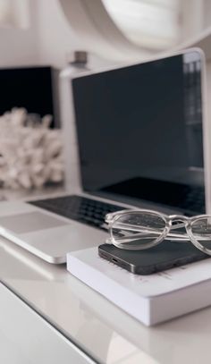 an open laptop computer sitting on top of a white desk next to glasses and a cell phone