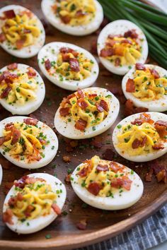 deviled eggs with bacon and chives on a wooden platter next to green onions