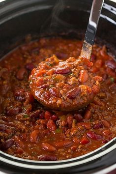 a slow cooker filled with chili and meat in the crock pot is being held by a ladle