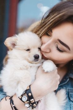 a woman holding a small white dog in her arms and kissing it's face