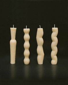 four candles are lined up next to each other on a black surface with one candle in the middle