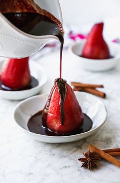 chocolate sauce being poured on two pears in small white bowls with cinnamon sticks and star anise