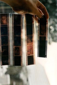 a hand holding two film strips in front of a window