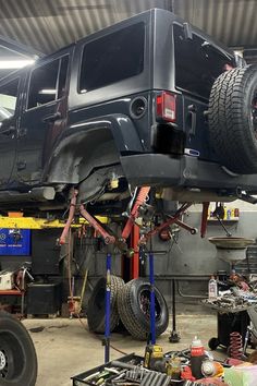 a jeep lifted up in a garage with other cars and tools on the ground around it