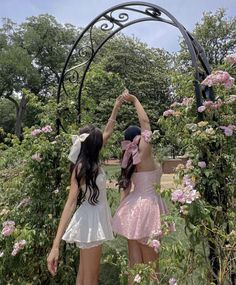 two young women standing in front of a garden arch