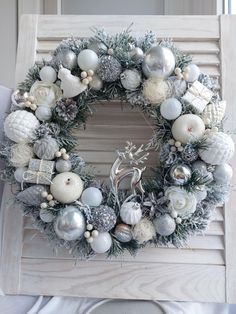 a christmas wreath with silver and white ornaments hanging from the side of a wooden slatted chair