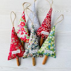 four small christmas trees are hanging from clothes pins on a white wooden background, with tags attached to them