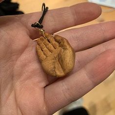 a hand holding a small wooden object in it's palm with a black cord