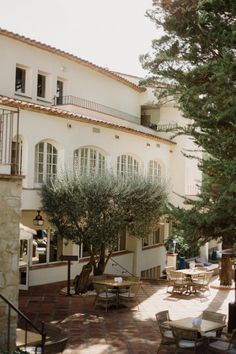 an outdoor patio with tables and chairs next to a tree in front of a large white building