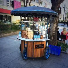 an ice cream cart sitting on the side of a road next to a tree and buildings