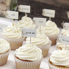 cupcakes with white frosting and name tags on them are displayed for sale