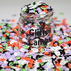 a jar filled with halloween buttons sitting on top of a white table next to a pile of purple and green sprinkles