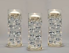 two clear glass vases with silver balls and lights on the bottom one has a lit candle in it