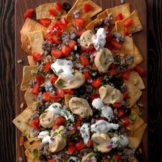 nachos with meat, cheese and tomatoes on a wooden platter next to chips