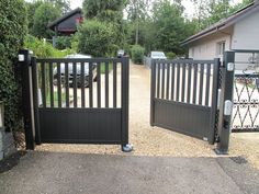 two black gates are open in front of a driveway with cars parked on the other side