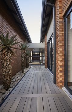 a wooden deck next to a brick building with glass doors and plants in the foreground