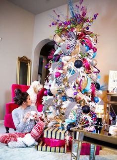 a woman sitting on the floor next to a christmas tree with decorations and gifts around it