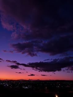 an airplane is flying in the sky at night with clouds and buildings behind it as the sun sets