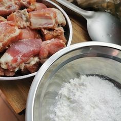 two bowls filled with meat next to other food items on a cutting board and spoons