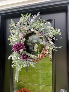 a wreath on the front door of a house with purple flowers and greenery hanging from it