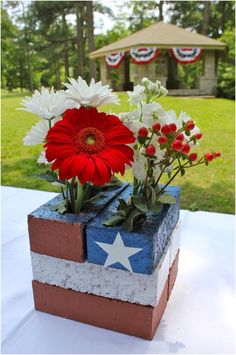 red, white and blue flowers are in a brick box on a table outside with an american flag decoration