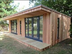 a small wooden building sitting in the middle of a field with lots of trees around it