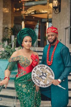 a man and woman dressed in traditional african garb standing on steps holding a decorative item