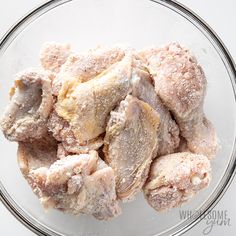 a glass bowl filled with chicken wings covered in powdered sugar on top of a white table