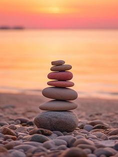 a stack of rocks sitting on top of a beach next to the ocean at sunset