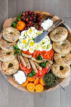 a platter filled with bagels, tomatoes, olives, cucumbers, and other foods