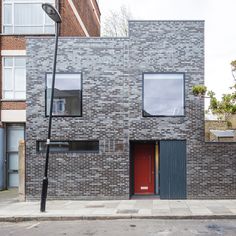 a brick building with two windows and a red door on the street corner in front of it