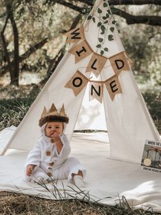 a baby wearing a crown sitting in front of a teepee