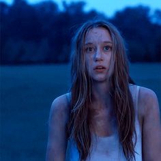 a woman standing in the middle of a field at night with blood on her face