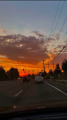 the sun is setting behind power lines and cars are driving down the street in front of them