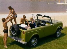 four people are standing in the back of an old green pickup truck at the beach