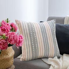 pink flowers in a vase sitting on a couch next to a pillow and throw pillows